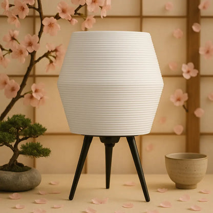 White textured lamp with black legs on a table with cherry blossoms and a pot in the background