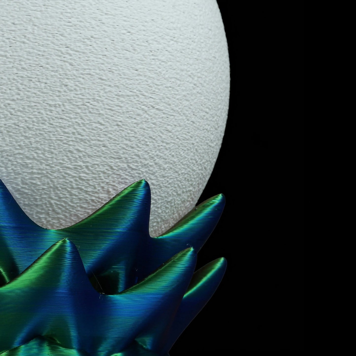 Close-up of a textured white lamp shade with a blue and green spiky base on a black background